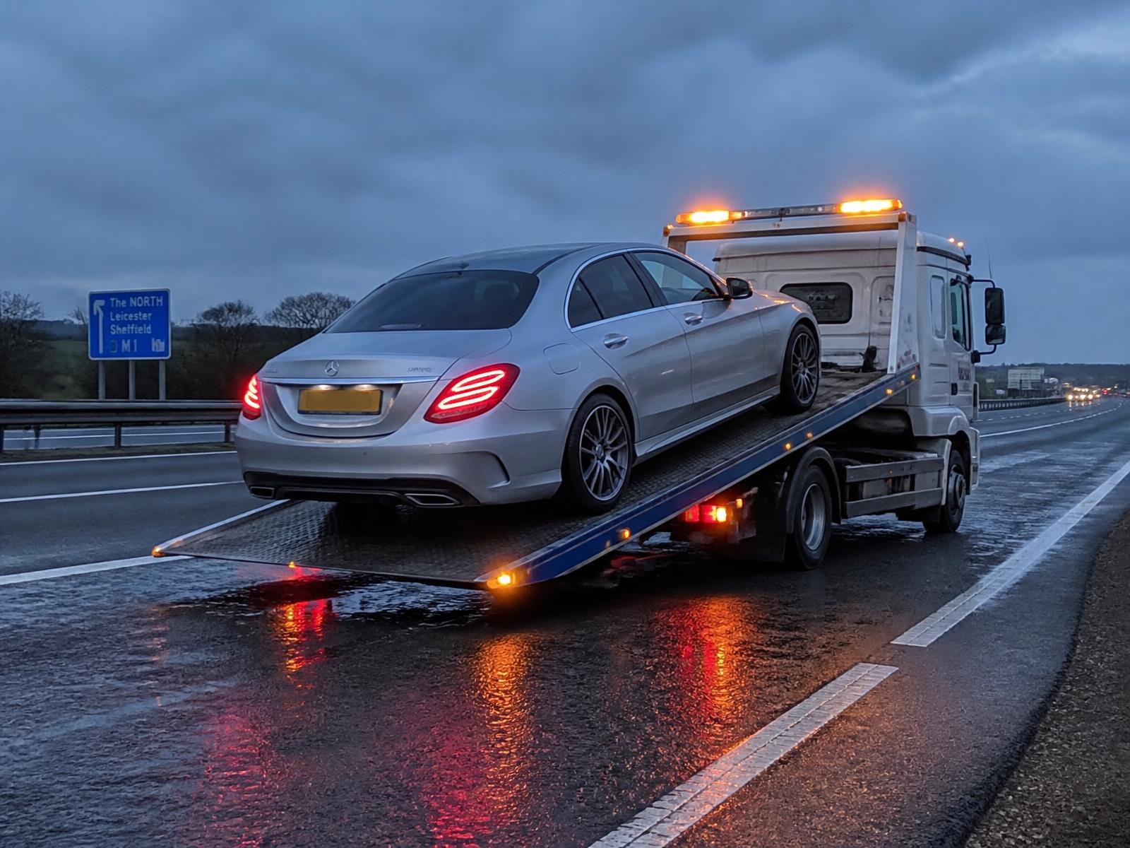 Modern UK recovery truck loading a luxury car on a British motorway hard shoulder